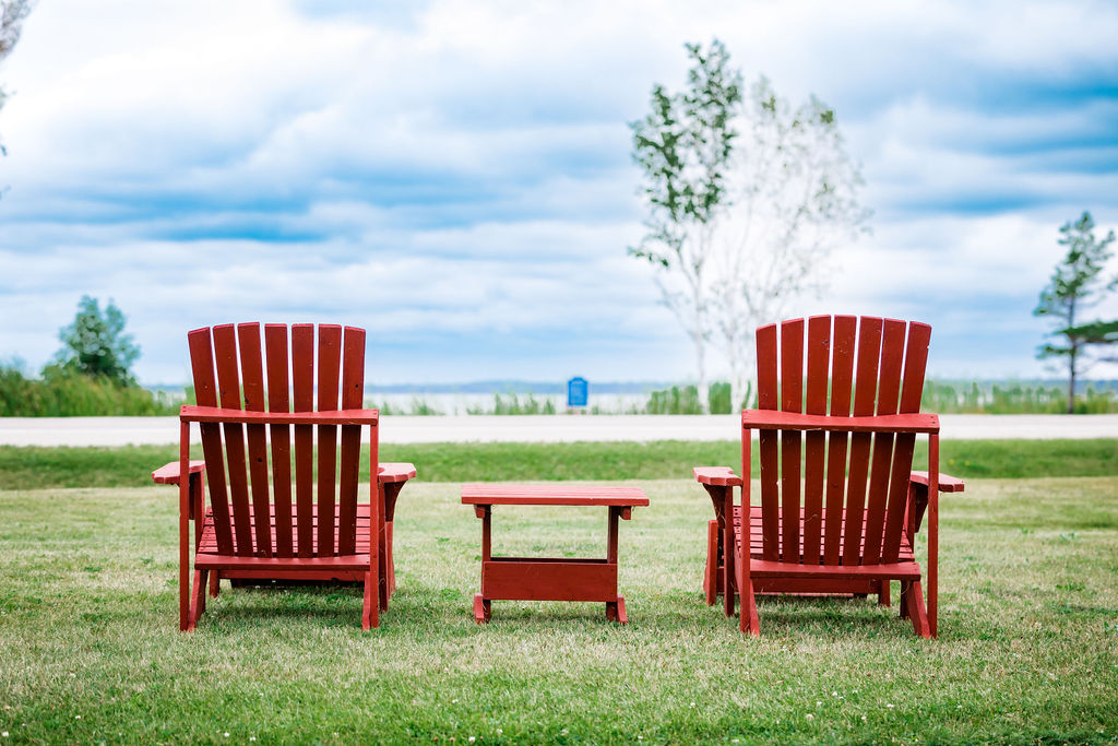 Two red Adirondack chairs and side table facing the lake