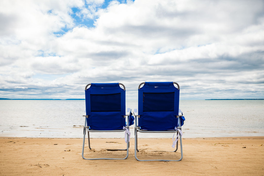 Pair of blue beach chairs from behind looking out at the water