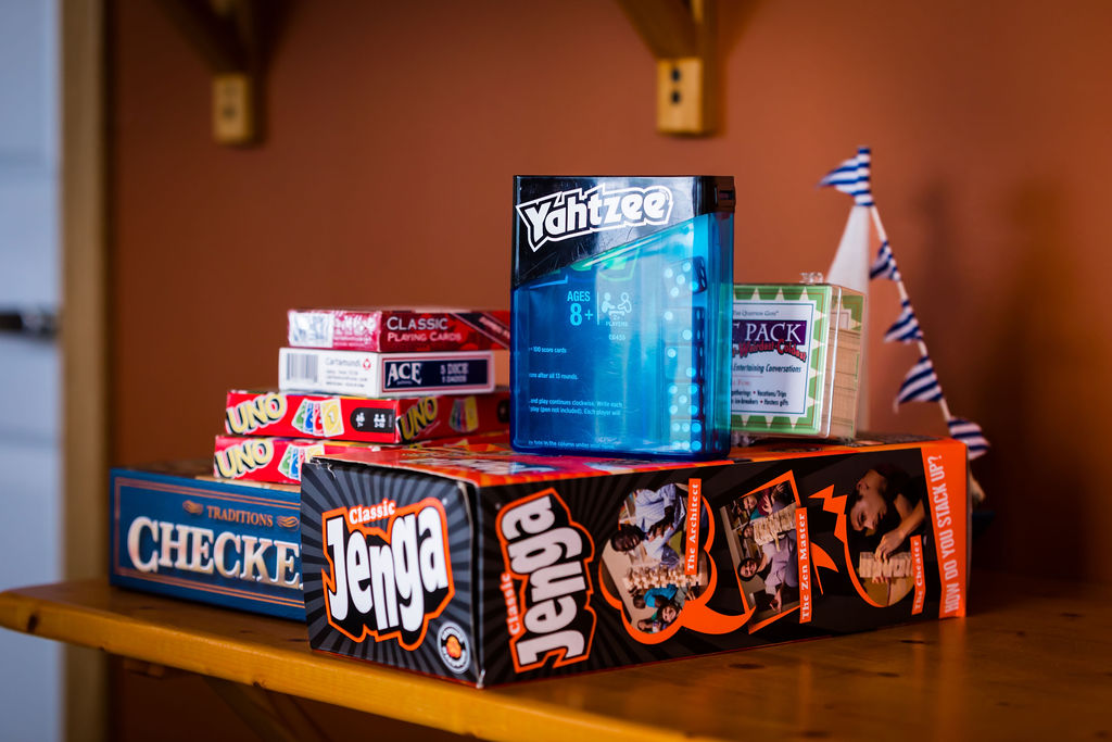 Stack of board games — Jenga, Yahtzee, Uno, Checkers — on a wooden shelf
