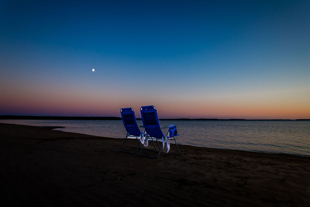 Beach chairs under moonrise at twilight