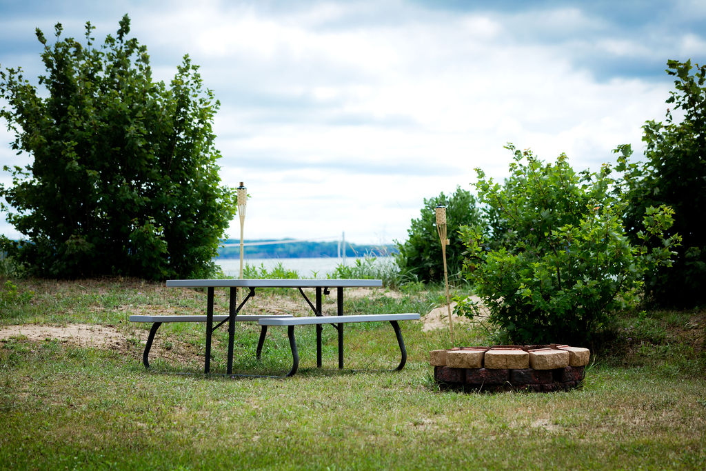 Picnic table and stone fire pit with tiki torches by the water