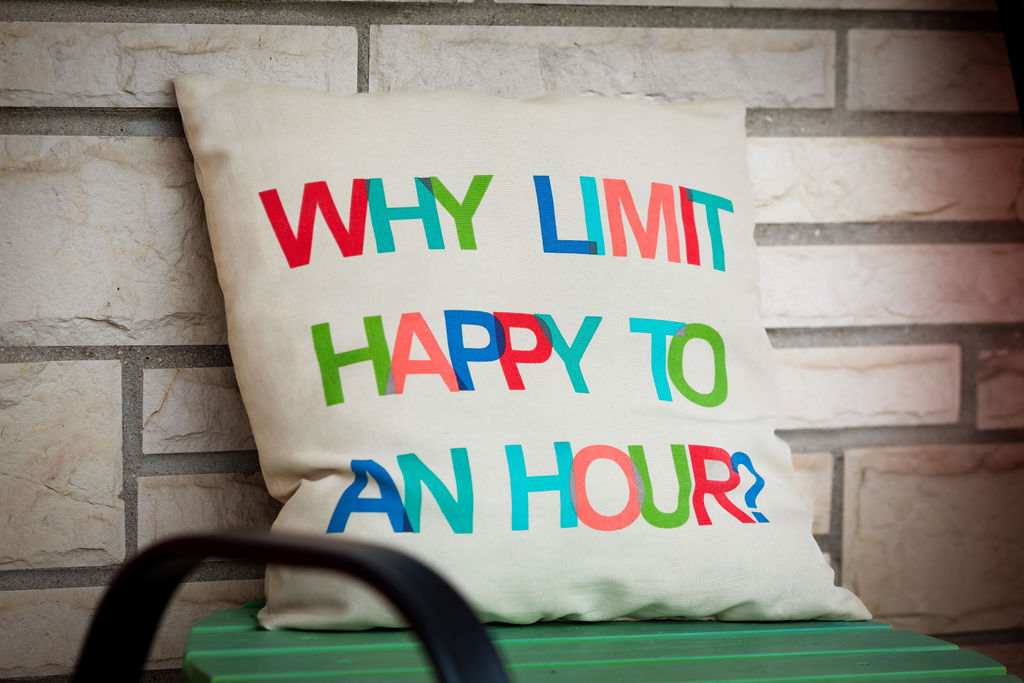 'Why limit happy to an hour?' pillow on a green porch bench