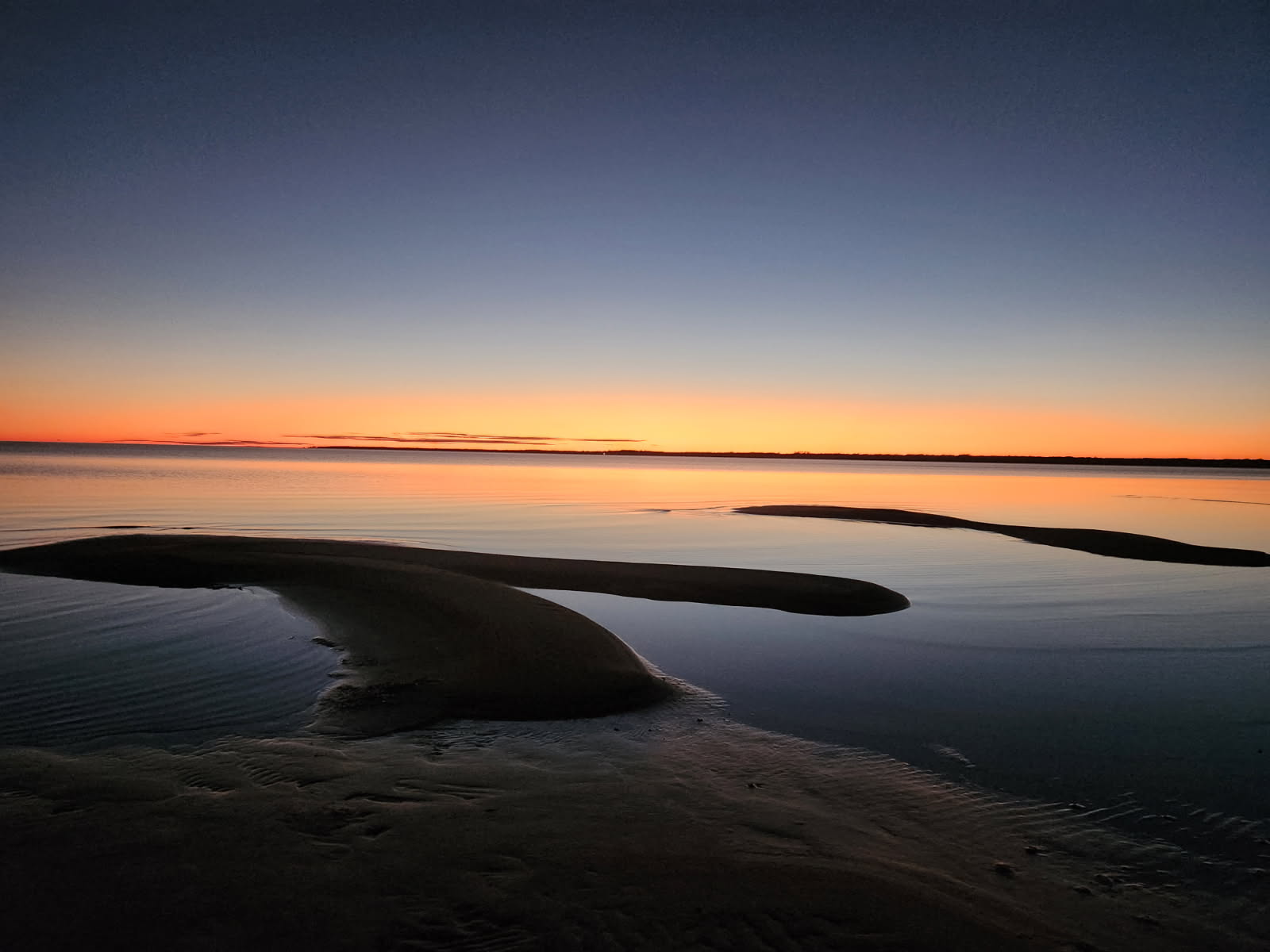 Curving sandbar revealed at low tide under a blue and orange dusk