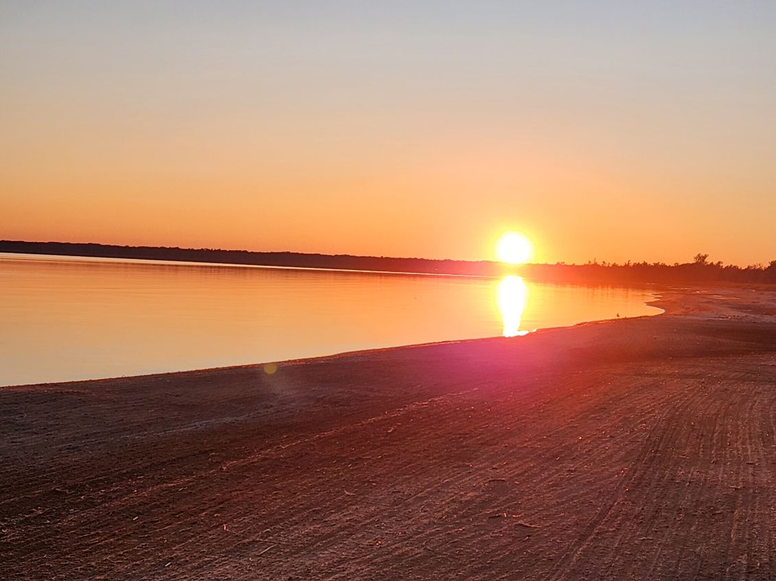 Brilliant sun setting over the calm lake with reflection on the sand