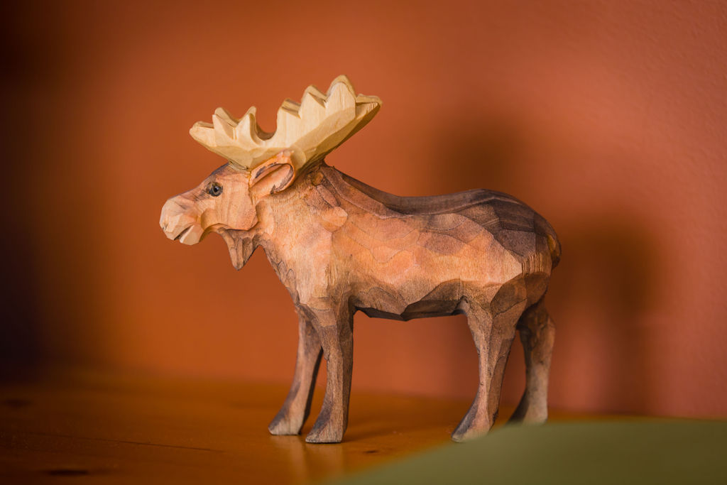 Hand-carved wooden moose figurine against a warm orange wall