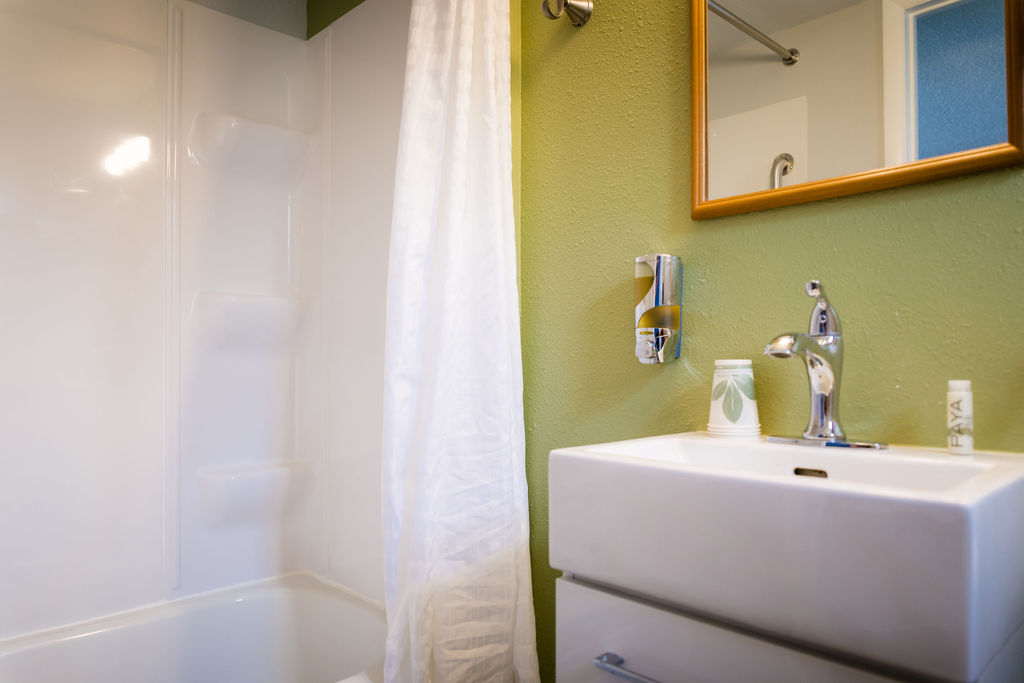 Tub-shower combo with white curtain beside the green-walled vanity