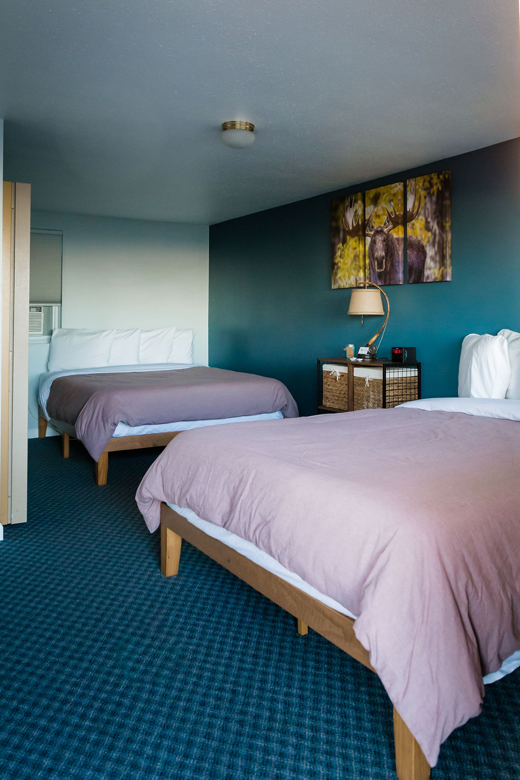 Two queen beds with teal accent wall and moose canvas art