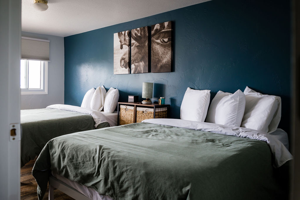 Two beds with sage green linens and moose triptych over teal wall
