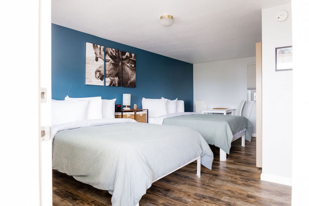 Spacious room with two beds, pale sage linens, and moose canvas