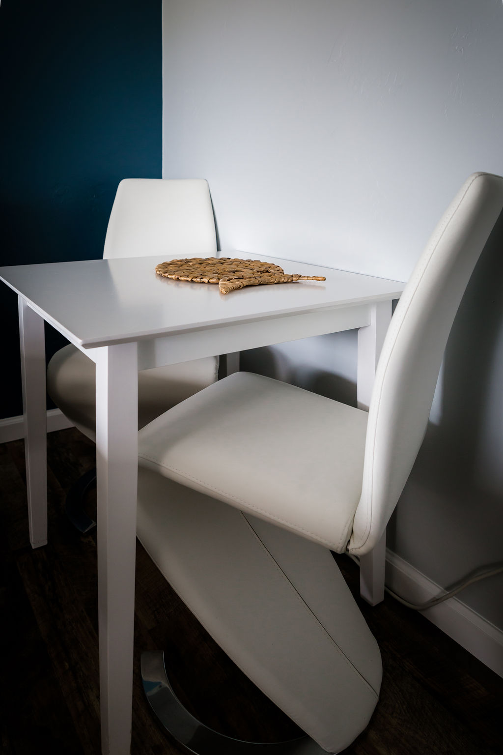 Small white dining table for two against teal accent wall